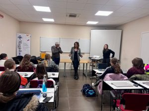 Un'aula con un uomo e due donne alla cattedra rivolti verso le studentesse sedute ai banchi durante l'incontro di Sinapsys a Girls Code it Better